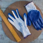 Blue and white nylon gardening gloves displayed on a wooden surface alongside a measuring ruler, ideal for hand protection during gardening tasks in Bangladesh
